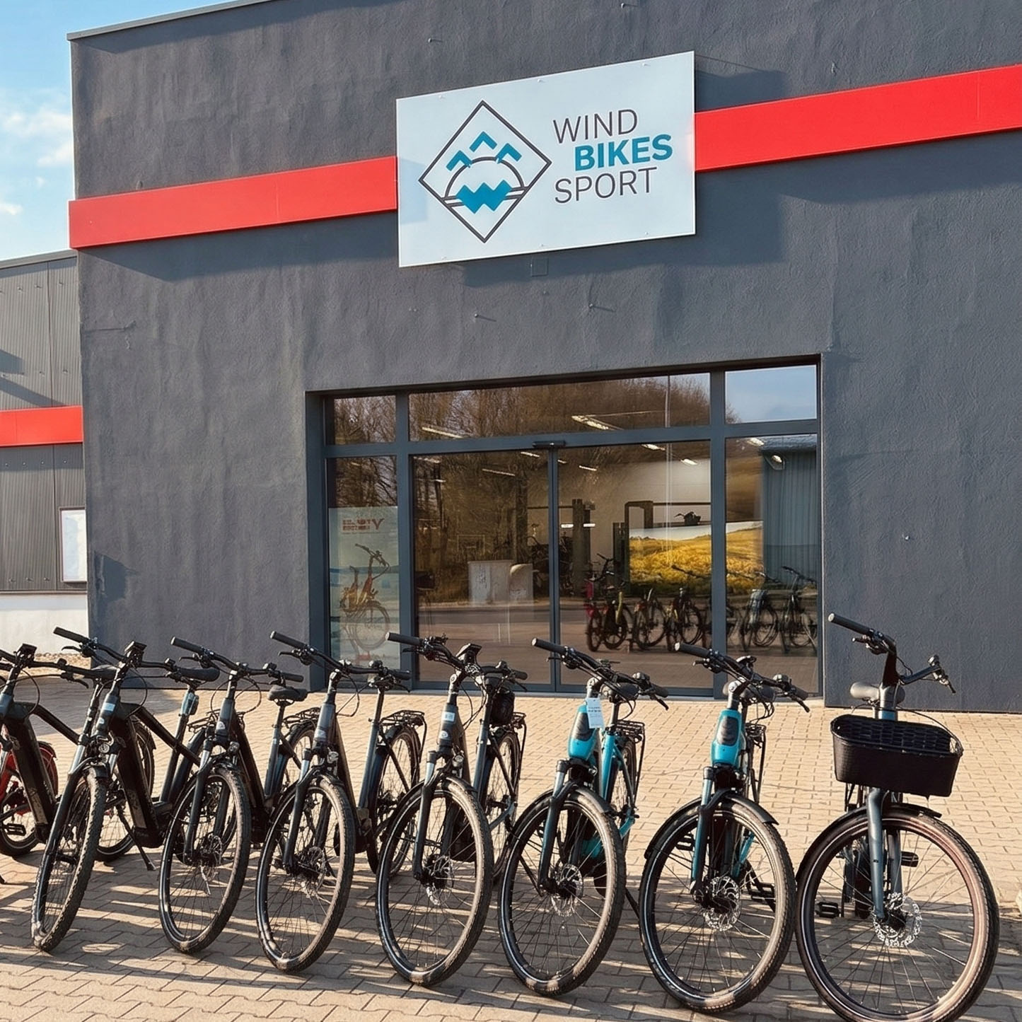 bikes1000x1000 - Windsport Fehmarn Mehrere Fahrräder und E-Bikes aufgereiht vor der Fassade des Geschäfts Wind Bikes Sport.