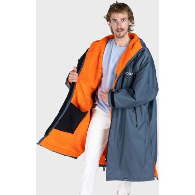 Ein Mann trägt einen blauen Dryrobe-Wechselmantel mit leuchtend orangem Innenfutter vor einem hellen Hintergrund.