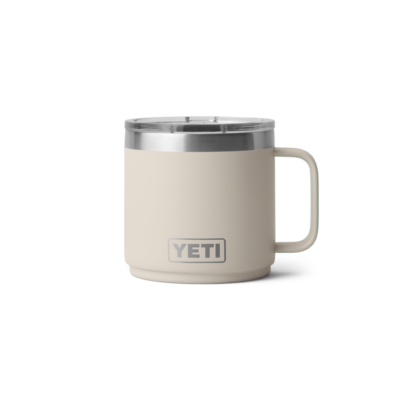 Ein beiger YETI Isolierbecher aus Edelstahl mit Griff und transparentem Deckel vor weißem Hintergrund.