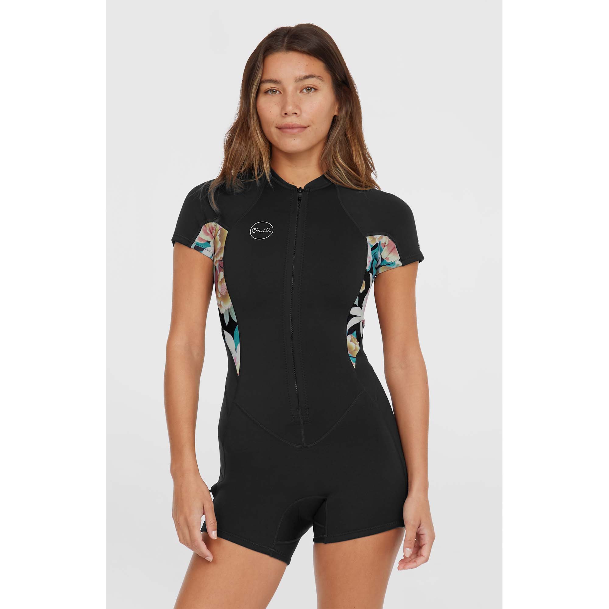 O'Neill Damen Bahia Neoprenanzug - Windsport Fehmarn Frau trägt einen schwarzen O'Neill Bahia Kurzarm-Neoprenanzug mit floralen Seiteneinsätzen vor weißem Hintergrund.