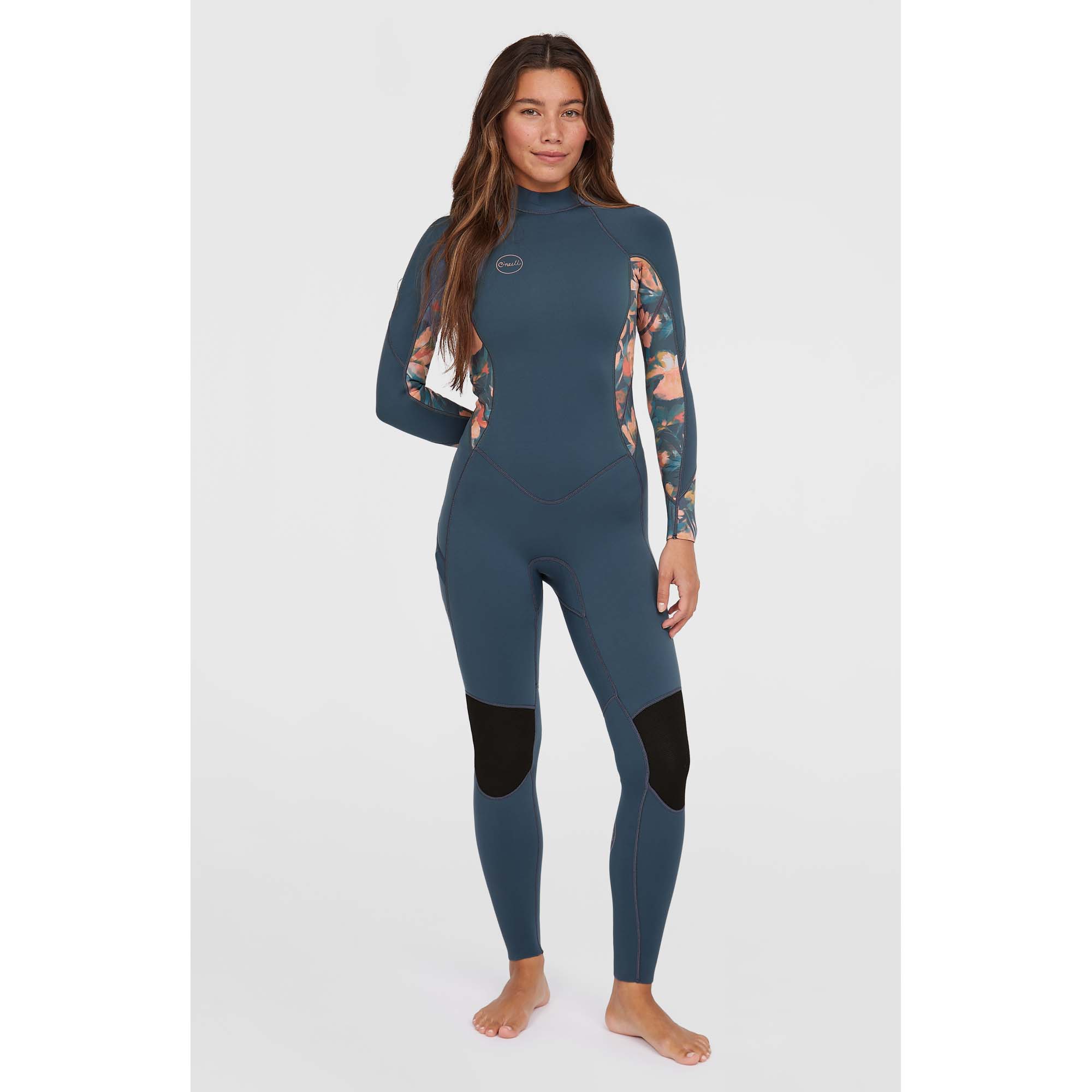 O'Neill Bahia Damen Neoprenanzug - Windsport Fehmarn Eine Frau trägt einen blauen O'Neill Bahia Damen-Neoprenanzug mit floralem Muster an den Ärmeln vor hellem Hintergrund.