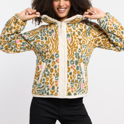 Eine lachende Frau trägt eine beige Fleecejacke mit buntem Leoparden- und Wellenmuster vor weißem Hintergrund.