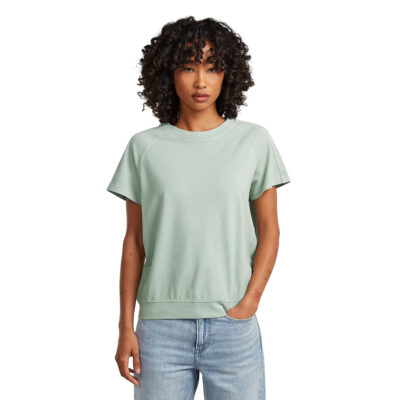 Frau mit lockigen Haaren trägt ein hellgrünes G-Star Raglan-T-Shirt zu einer blauen Jeans.